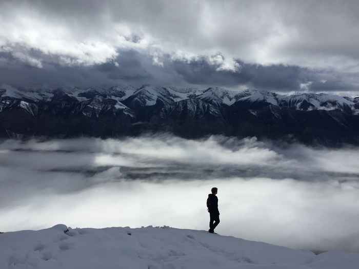 Man walking alone through a black-white-gray landscape with mountains and clouds.