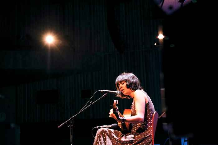Student seated playing guitar and singing in microphone