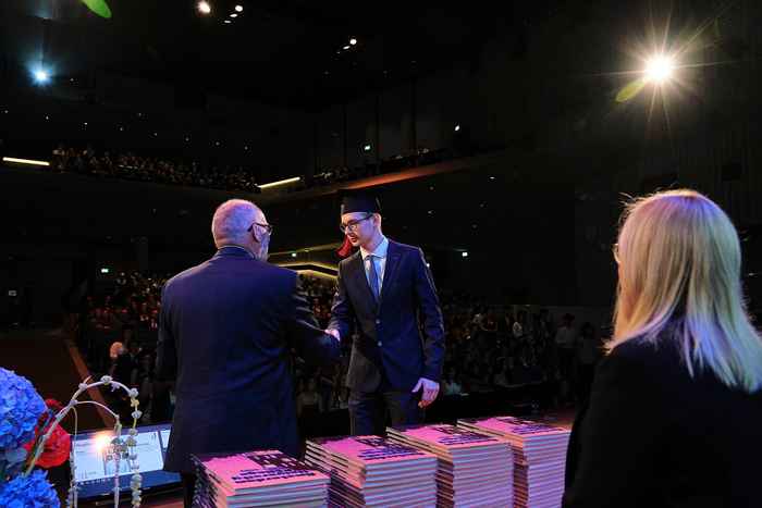 Student receiving ceremonial certificate on stage, view from behind
