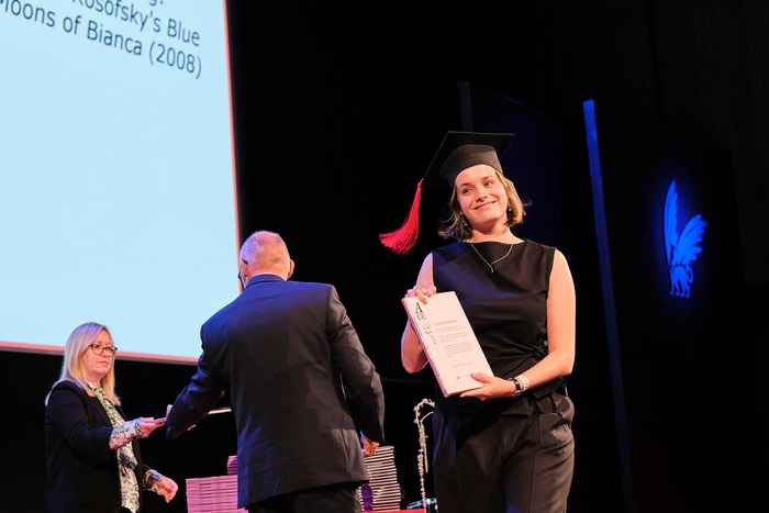 Student receiving ceremonial certificate on stage, facing audience